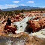 A scenic view of Gunlock State Park featuring a tranquil reservoir surrounded by red rock cliffs and desert landscapes.