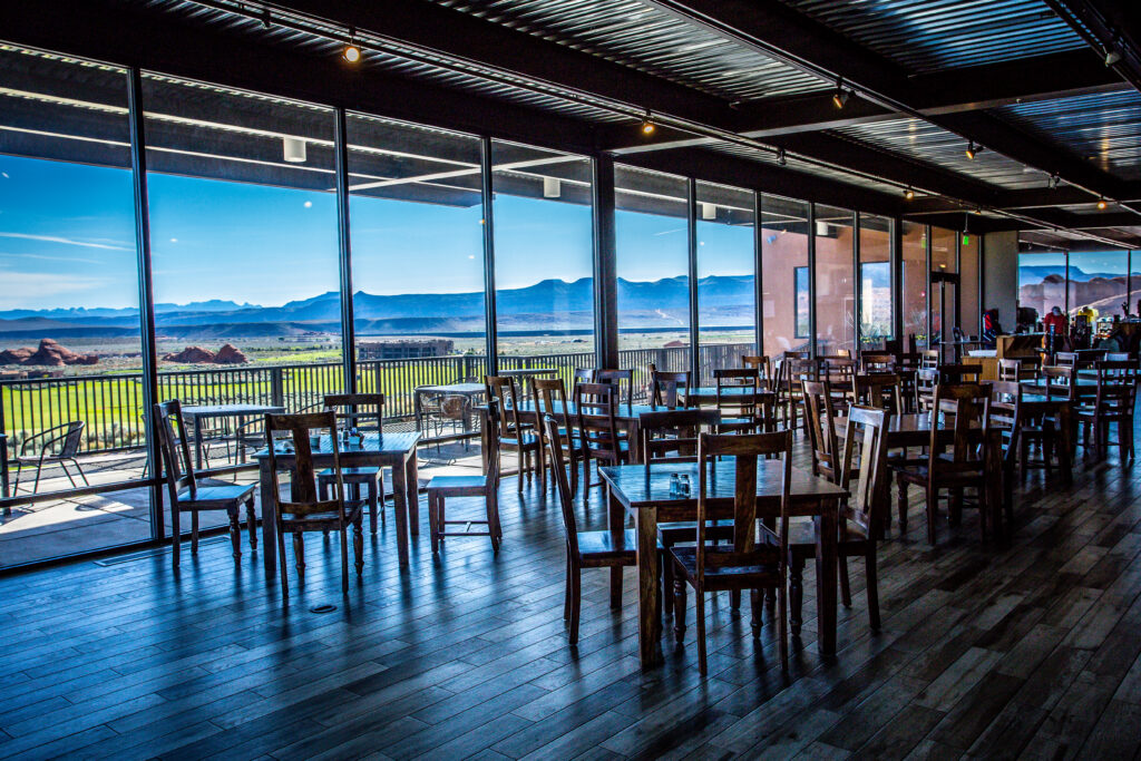 An interior dining hall with wooden tables and floor-to-ceiling windows overlooking a desert golf course and mountains, illustrating the modern amenities of premier corporate retreat venues St. George Utah offers.